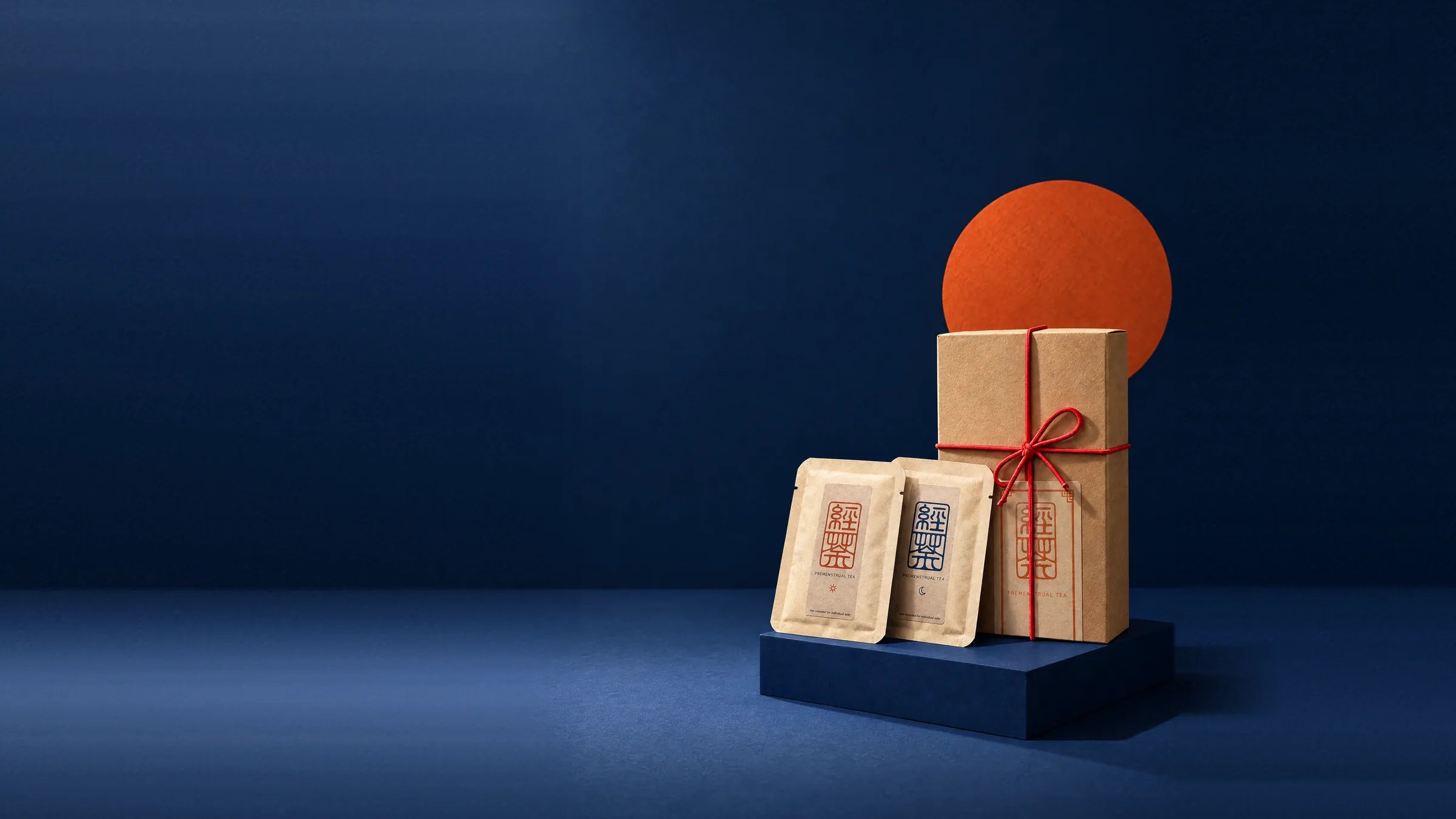 The Premenstrual Tea box tied with red cord, with a morning and an evening sachet, in front of a vermilion sun